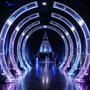 Curved Arch Hire | Osmic Productions Glowing Circular Arches Form a Tunnel at a Dark Indoor Event Space with Guests in the Distance Behind the Arches Far End of the Walkway.