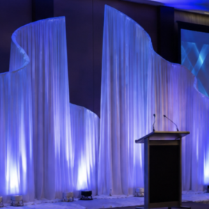 Screenshot 20260902 at 53013 Pm | Osmic Productions Blue-lit Conference Stage Featuring Flowing White Fabric Sculptures, a Central Podium, and a Screen That Says 'leadership in Action' — Annual Conference 2005.