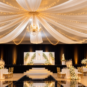 Ceiling Drape Image Oct 20 2026 102222 Am2 | Osmic Productions Elegant Wedding Altar with White Drapes Radiating from a Central Point, Chandelier, and Floral Arches Surrounding a White Sofa on a Raised Platform; Warm String Lights Create a Golden Glow.