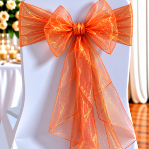 Organza Orange Shimmer | Osmic Productions White Chair Decorated with a Large Orange Organza Bow Tied at the Back, with a Softly Blurred Reception Backdrop of Flowers and Candles in the Background.