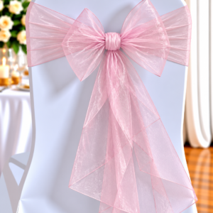 Organza Pink | Osmic Productions White Chair Tied with a Large Pink Sheer Bow for an Event, with a Floral Table Setup in the Blurred Background.