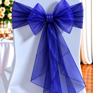 White chair with a royal blue organza bow tied around the back, at a decorated event table.