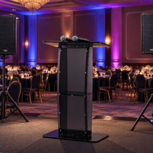 Podium with two wireless mics on stage flanked by two speaker stands in a decorated banquet hall with purple and blue uplighting