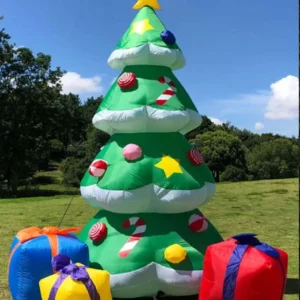 Inflatable green Christmas tree with star topper and ornaments, set in a grassy park beside oversized gift boxes.